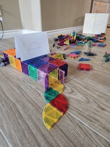 A small structure built out of magnatiles, with a folded sheet of paper on top with the letter A written on it in crayon.
